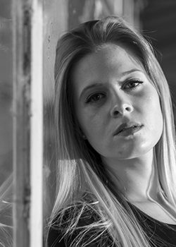 Young woman leaning against a window and looking at the camera.