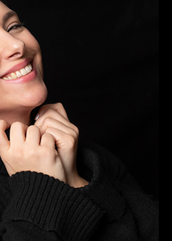 Portrait of a laughing young woman with black sweater against a black background.